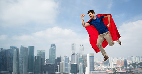 Image showing man in red superhero cape flying in air over city