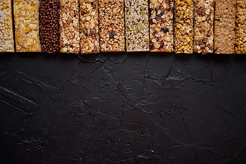 Image showing Various healthy granola bars placed in a row on black stone table