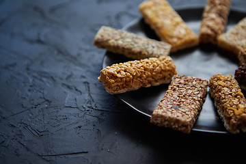 Image showing Different kind of granola fitness bars placed on black ceramic plate on a table