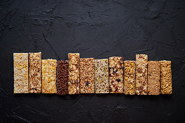 Image showing Various healthy granola bars placed in a row on black stone tabl