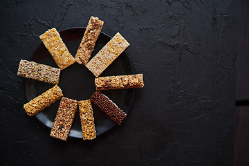 Image showing Different kind of granola fitness bars placed on black ceramic plate on a table