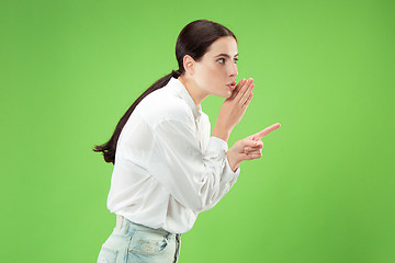 Image showing The young woman whispering a secret behind her hand over green background