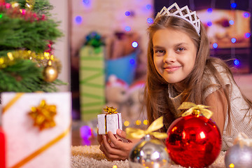 Image showing The girl is lying at the Christmas tree and holding a small gift
