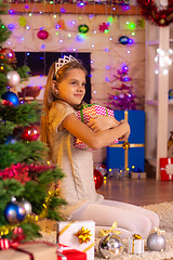 Image showing Ten-year-old girl sits at the Christmas tree and hugs a gift