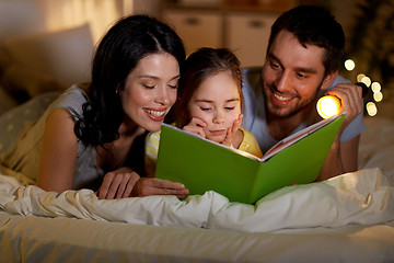 Image showing happy family reading book in bed at night at home