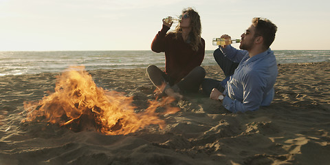 Image showing Loving Young Couple Sitting On The Beach beside Campfire drinkin