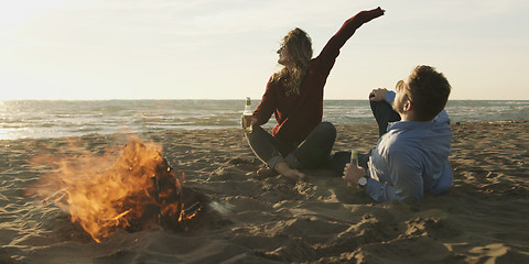 Image showing Loving Young Couple Sitting On The Beach beside Campfire drinkin