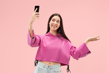 Image showing Portrait of a happy smiling casual girl showing blank screen mobile phone isolated over pink background