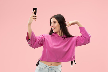 Image showing Portrait of a happy smiling casual girl showing blank screen mobile phone isolated over pink background