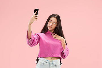 Image showing Portrait of a happy smiling casual girl showing blank screen mobile phone isolated over pink background