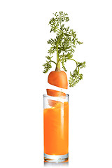Image showing Carrot root falls in a glass of fresh juice.