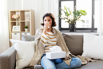 Image showing sick woman blowing nose in paper tissue at home