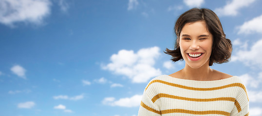 Image showing happy smiling woman winking over blue sky