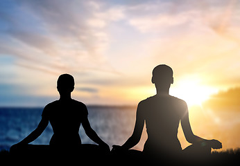 Image showing couple doing yoga in lotus pose over sea sunset