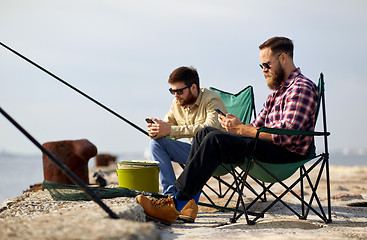 Image showing friends with smartphones fishing on pier at sea