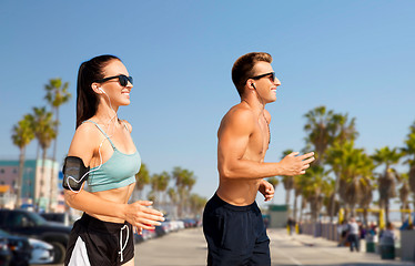 Image showing couple with phones and arm bands running on beach