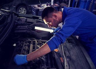 Image showing mechanic man with lamp repairing car at workshop