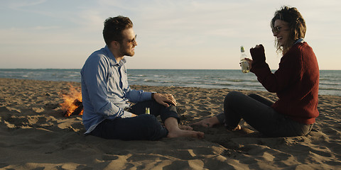 Image showing Loving Young Couple Sitting On The Beach beside Campfire drinkin