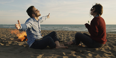 Image showing Loving Young Couple Sitting On The Beach beside Campfire drinkin