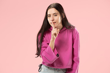 Image showing The young woman whispering a secret behind her hand over pink background