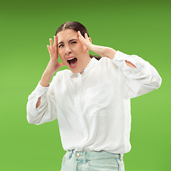 Image showing The young emotional angry woman screaming on green studio background