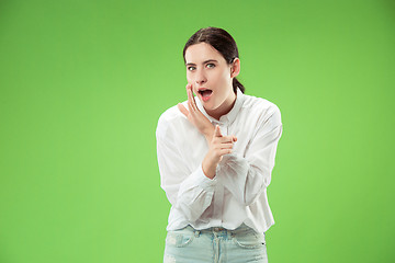 Image showing The young woman whispering a secret behind her hand over green background