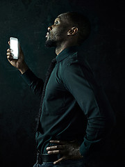 Image showing Studio shot of young serious black African man thinking while talking on mobile phone against black background