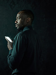 Image showing Studio shot of young serious black African man thinking while talking on mobile phone against black background