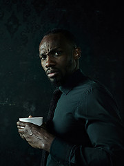 Image showing Stylish young black man with cup of coffee posing on dark background.