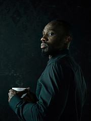 Image showing Stylish young black man with cup of coffee posing on dark background.