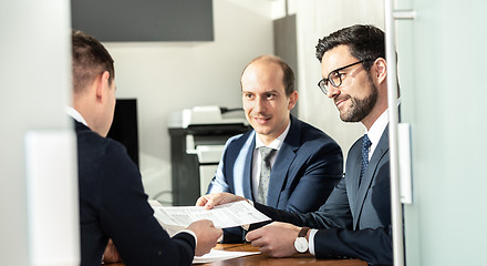 Image showing Group of confident successful business people reviewing and signing a contract to seal the deal at business meeting in modern corporate office.