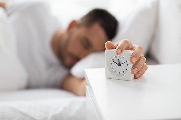 Image showing close up of man in bed reaching for alarm clock