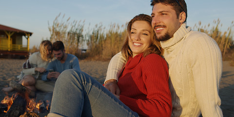 Image showing Loving Young Couple Sitting On The Beach beside Campfire drinkin