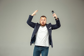 Image showing Young man with microphone on gray background, leading with microphone