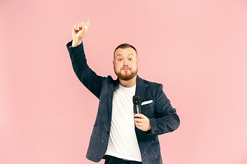 Image showing Young man with microphone on pink background, leading with microphone