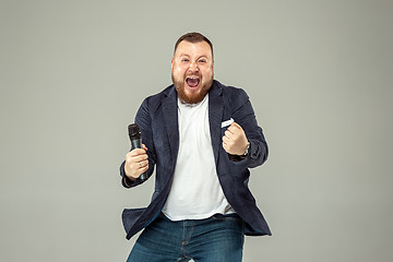 Image showing Young man with microphone on gray background, leading with microphone