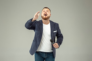 Image showing Young man with microphone on gray background, leading with microphone