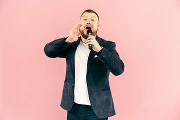 Image showing Young man with microphone on pink background, leading with microphone