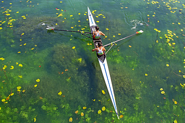 Image showing Two young athletes rowing team on green lake