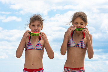 Image showing Two girls eat watermelon on the beach against the cloudy sky