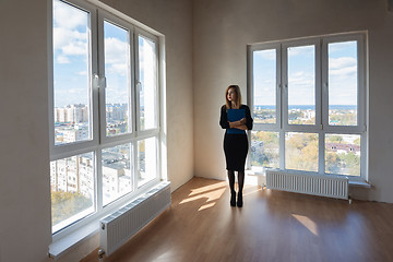 Image showing Girl realtor with a folder stands at the big windows of a spacious apartment