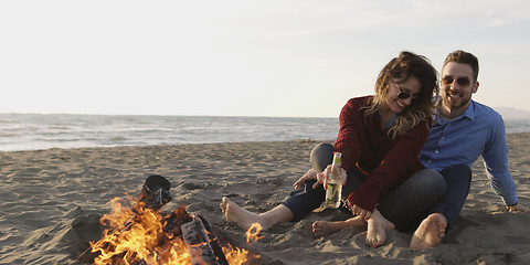 Image showing Loving Young Couple Sitting On The Beach beside Campfire drinkin