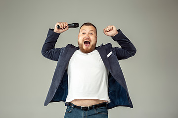 Image showing Young man with microphone on gray background, leading with microphone