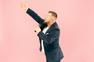 Image showing Young man with microphone on pink background, leading with microphone