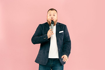 Image showing Young man with microphone on pink background, leading with microphone