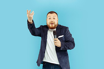 Image showing Young man with microphone on blue background, leading concept