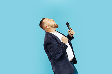 Image showing Young man with microphone on blue background, leading concept