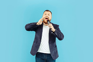 Image showing Young man with microphone on blue background, leading concept