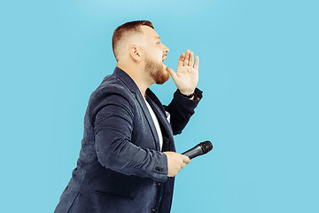 Image showing Young man with microphone on blue background, leading concept