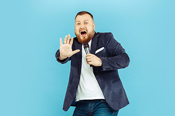 Image showing Young man with microphone on blue background, leading concept